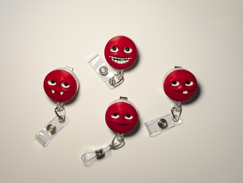 Four red retractable badge reel clips with cartoon face details, arranged on a light gray background.