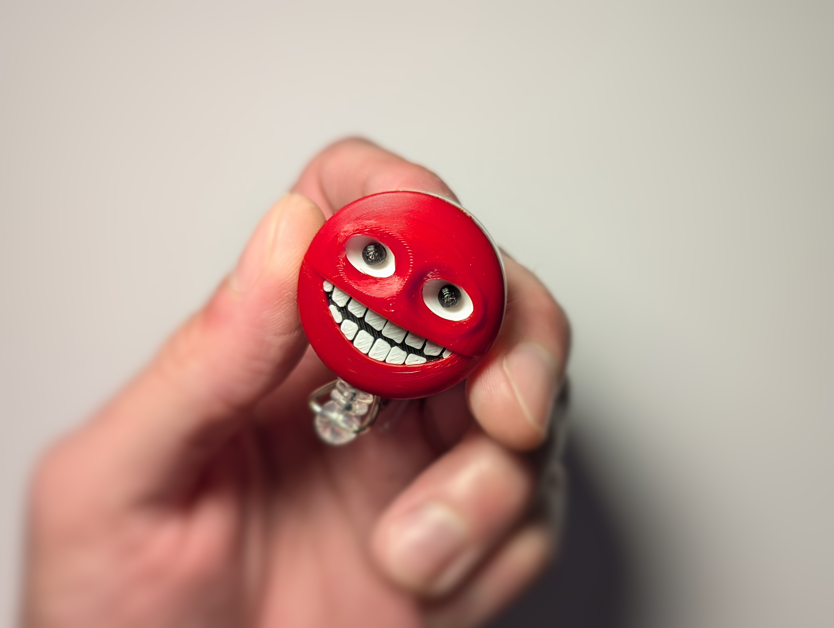 A hand holding a small red smiley face badge reel accessory against a plain light gray background.